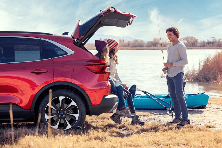 Family fishing by the lake with a red SUV in the background.